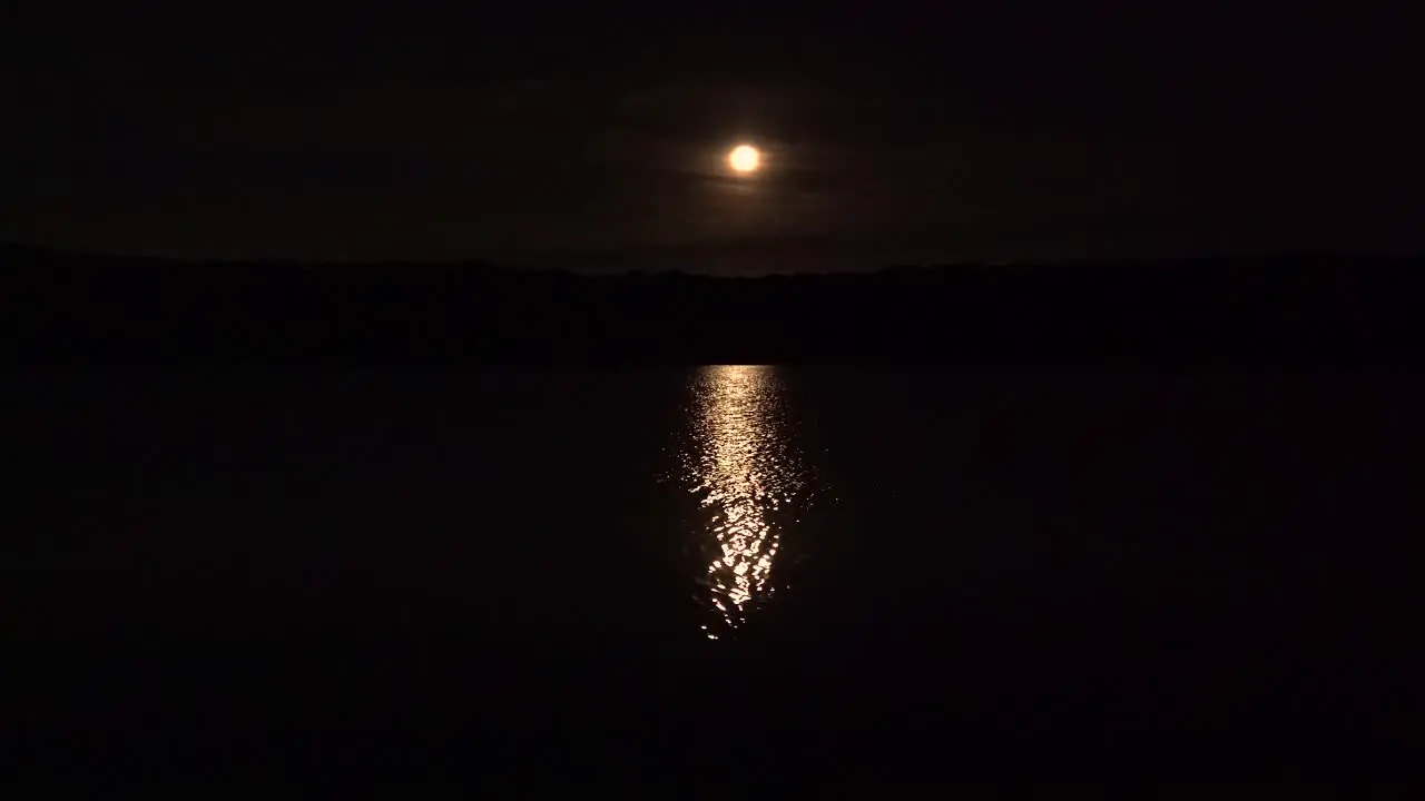 full harvest moon with reflection over a lake with forest silhouette 4k