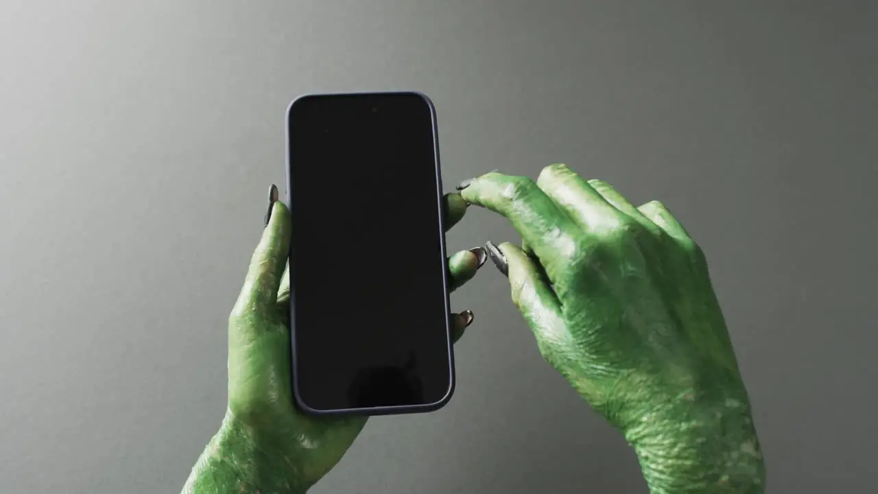 Video of halloween green monster hands holding smartphone with copy space on grey background