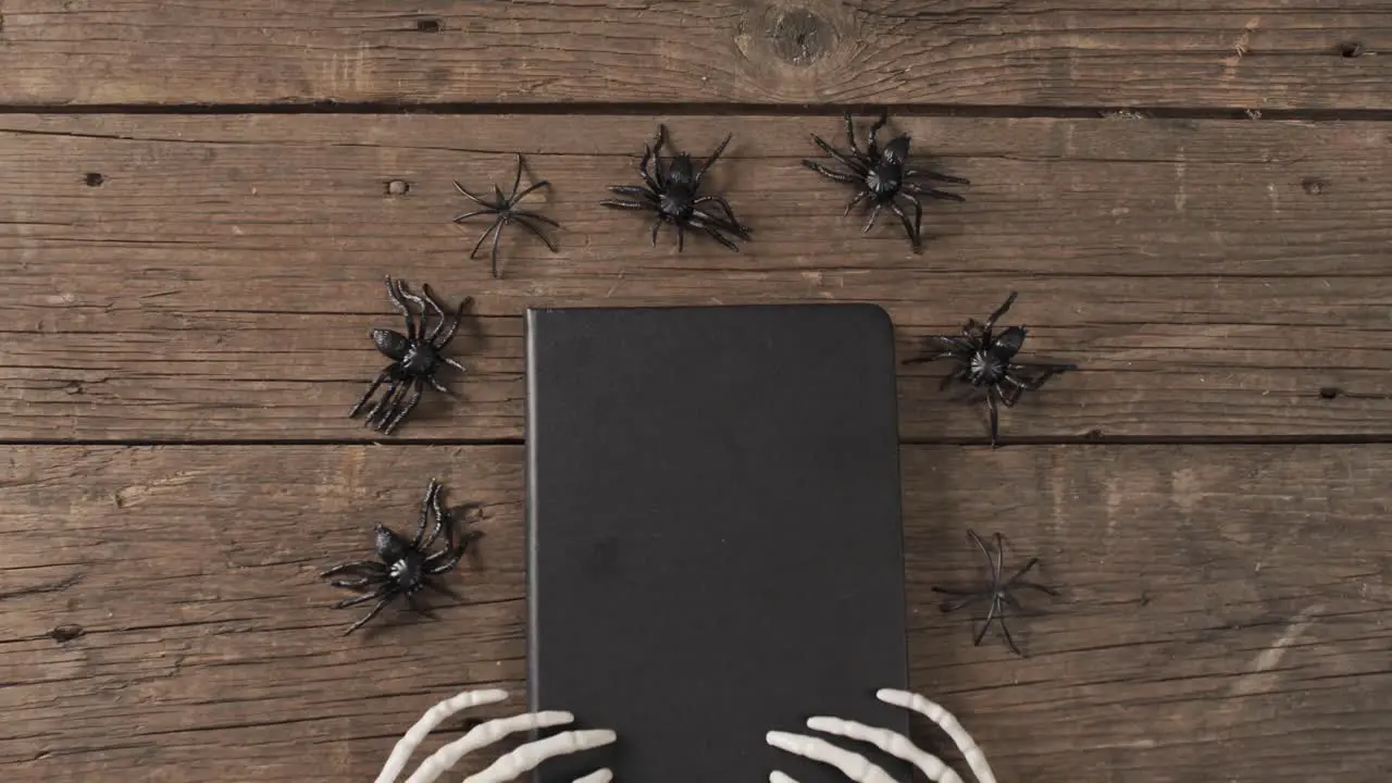 Video of halloween skeleton hands notebook and spiders with copy space on wooden background