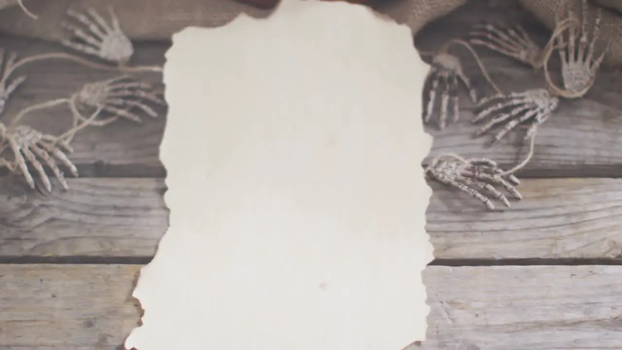 Paper with copy space against skeleton hands and pumpkins on wooden surface