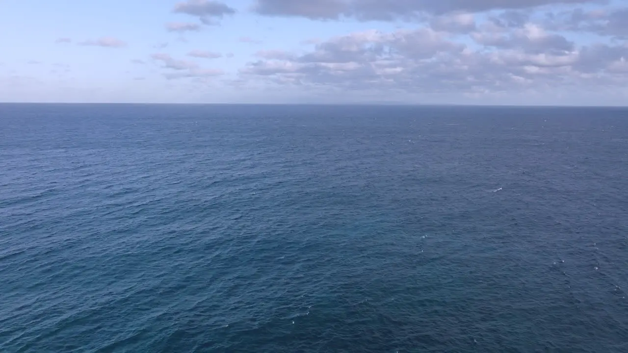 Aerial of Pacific Ocean with pull back and tilt down over beautiful turquoise blue waves off the coast of Oahu Hawaii