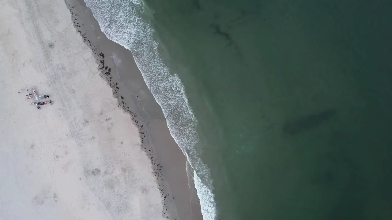 Ocean waves crash while beachgoers relax and watch the sun set