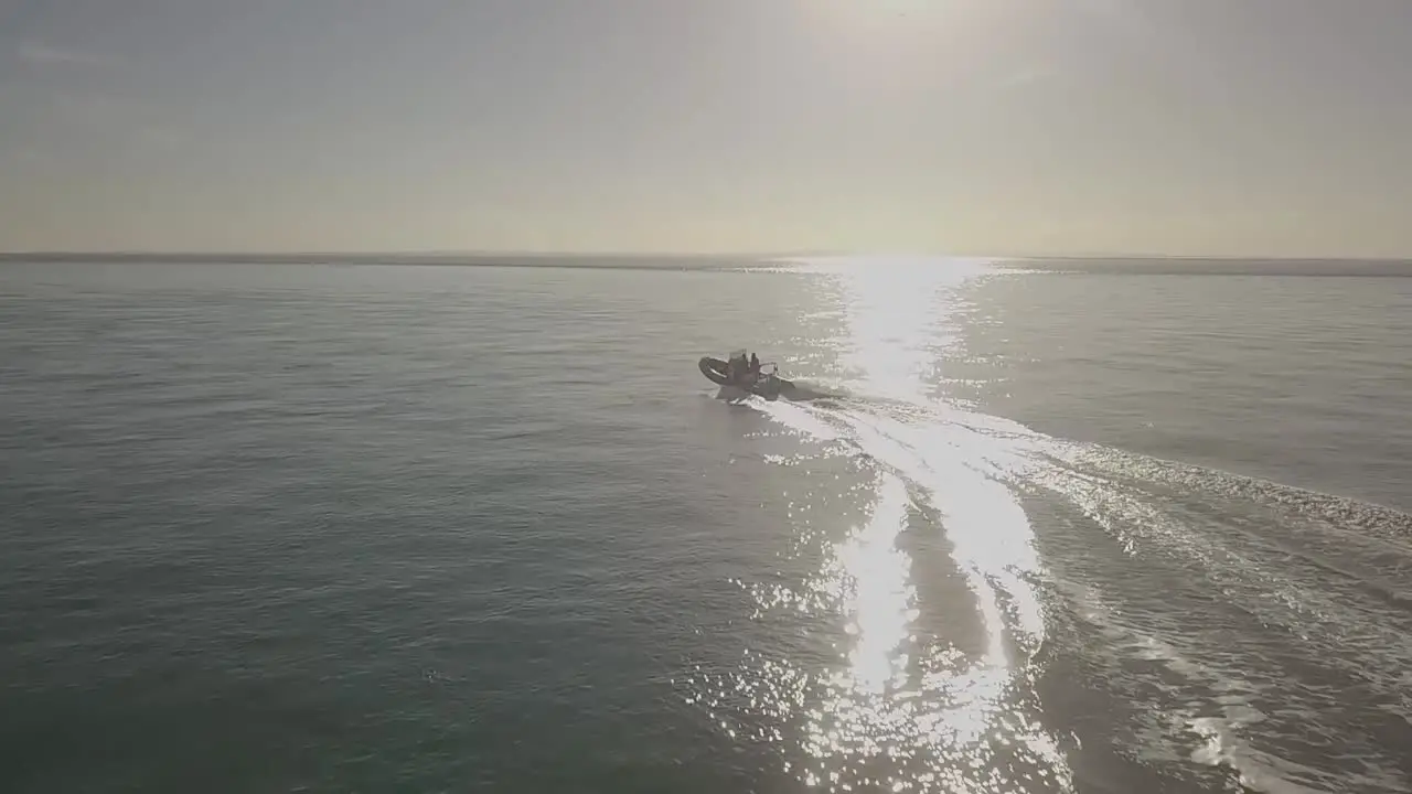 Slow motion aerial drone footage of motor boat travelling towards sun and then turning at high speed across smooth ocean water