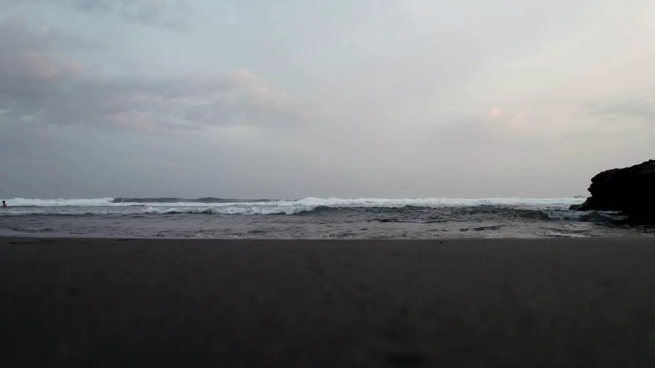 4K footage of a dog running by black sandy beach foamy waves rolling onto coast