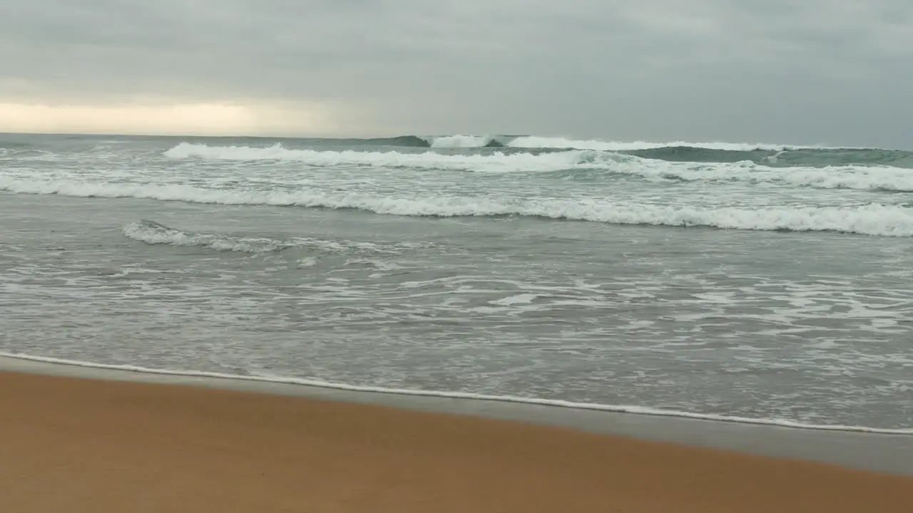 Waves breaking onto sandy beach cloudy skies in background