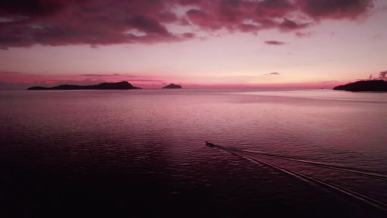 boat traveling at sea during red post sunset with islands in the background