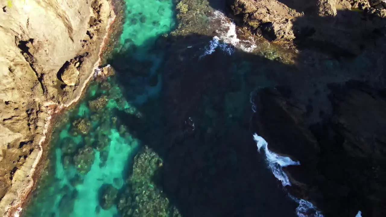 Flying over crystal blue waters and rocky reef breaking onto seashore of pacific island