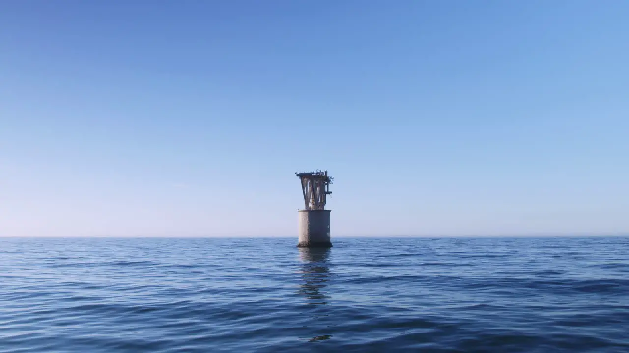 Drone flying near the water and moving closer to an abandoned structure in the middle of the sea