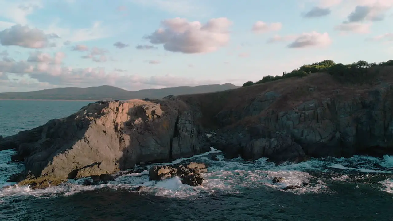 Aerial pan shot of big seashore cliffs and waves with drone at sunset