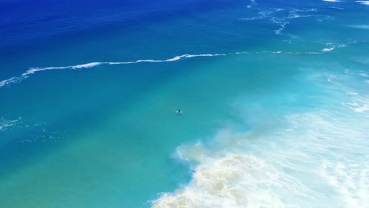 Surfer alone in turquoise ocean waiting on waves high angle drone shot