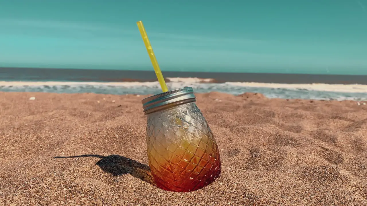 Summer tropical pina colada cocktail in a pineapple glass on a beautiful beach with the sea waves rolling in from the ocean