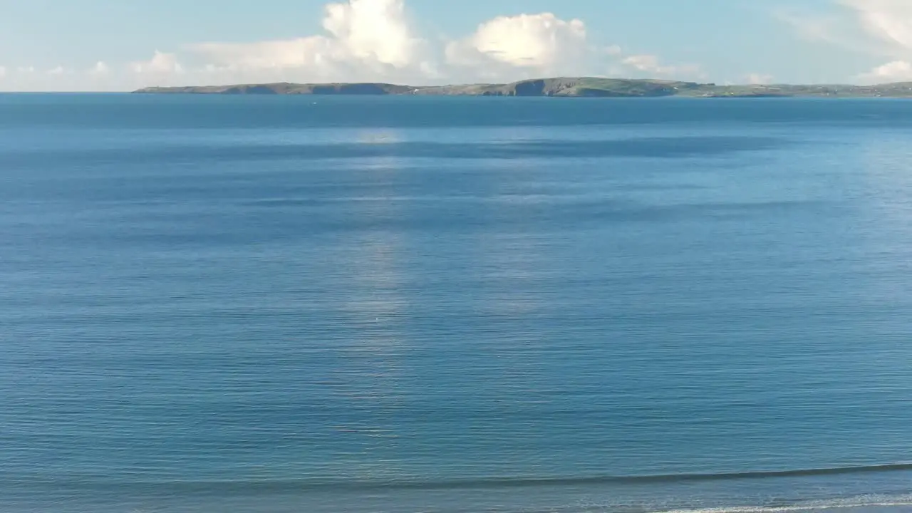 Calm winter ocean and distant Irish coast with white clouds on a clear morning sky