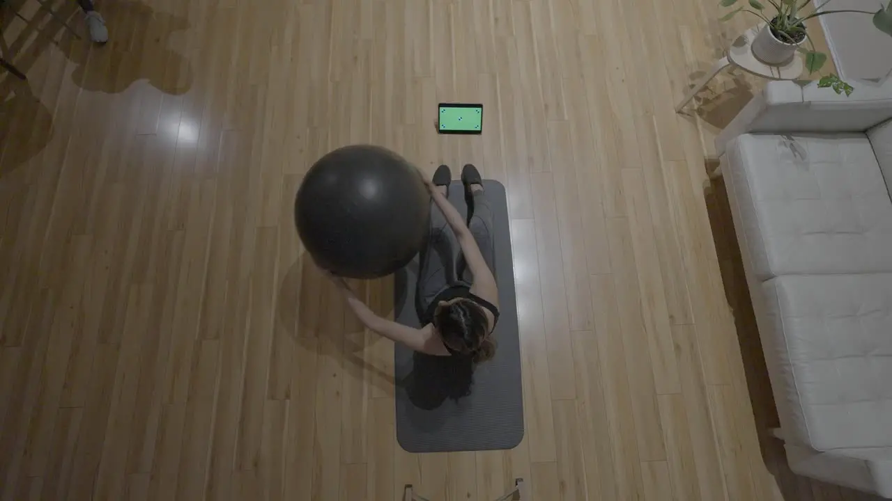 An overhead static shot ofan Hispanic woman doing an work outs with a medicine ball in front of her green screened tablet