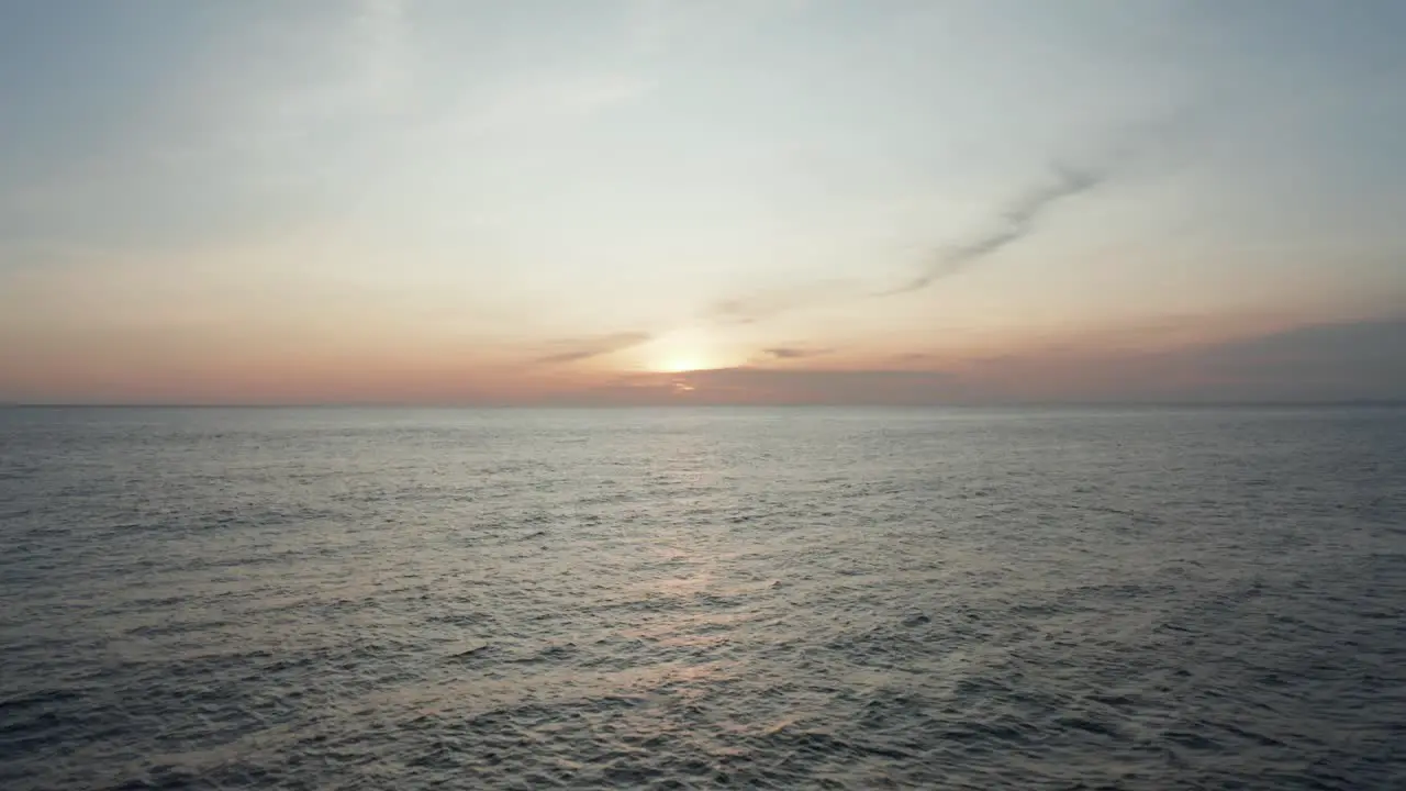 Low aerial drone video flying over water towards sun at sunset sunrise