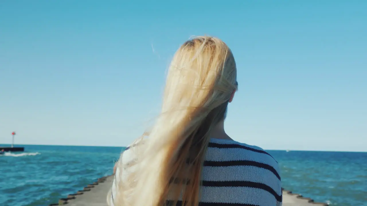 A Woman With Long Hair Strolls Along The Pier The Wind Ruffles Her Hair Back View