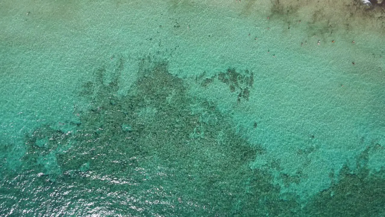 Aerial view of the calm turquoise ocean and crowded beach on a clear sunny day in 4K flying over tropical crystal clear waters