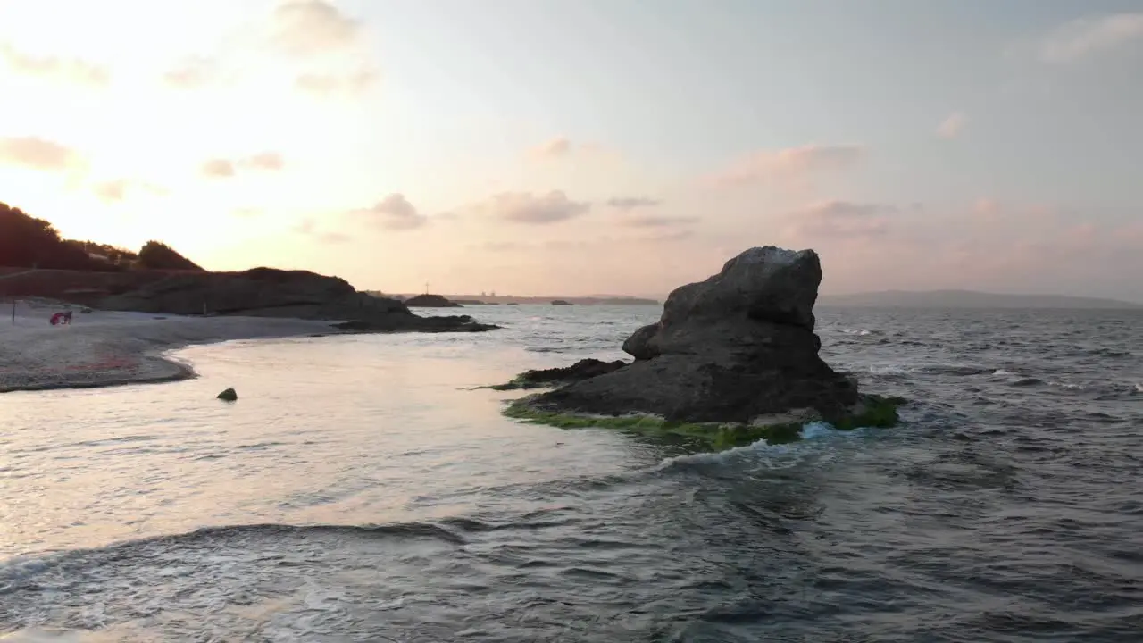 Low aerial parallax shot around cliff in the sea close to the beach at sunset