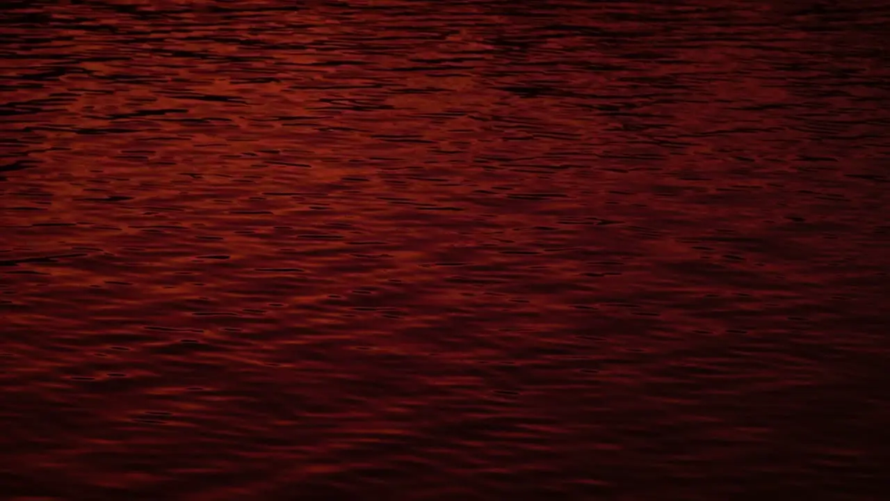 Abstract red sunset dusk reflection on rippling lake water slow motion