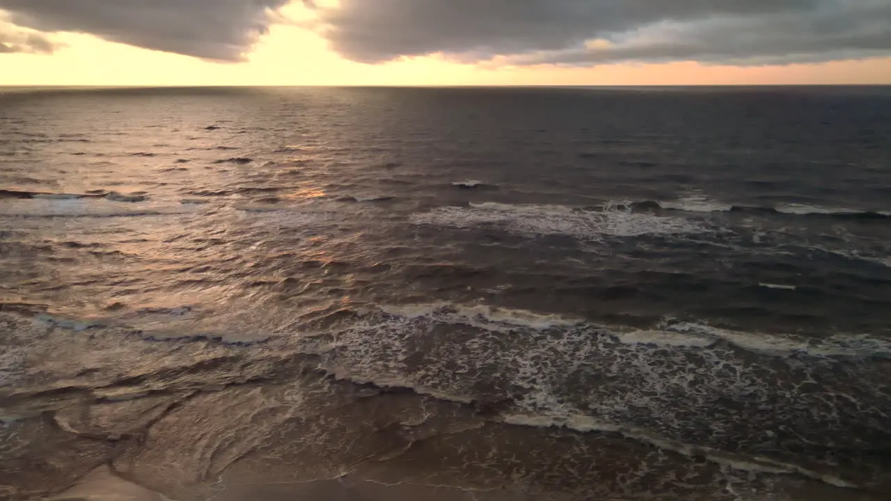 Aerial shot of beautiful sunset over crashing ocean waves on sandy beach