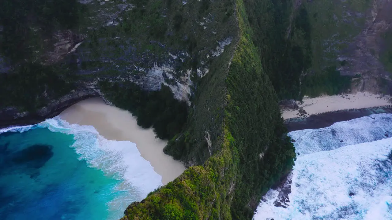 Beautiful cinematic aerial shot of exotics mountains crystal clear blue water and waves hitting the beach of Nusa Penida Kelingking