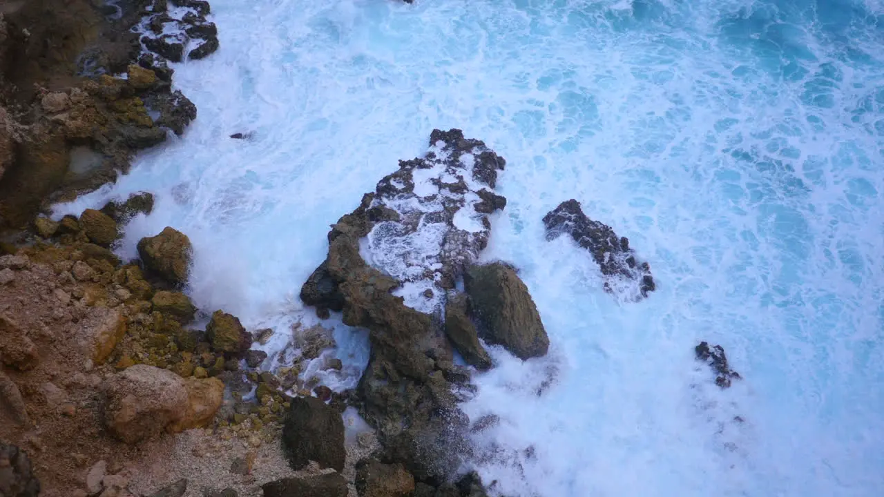 View from top of a cliff down to crashing blue waves