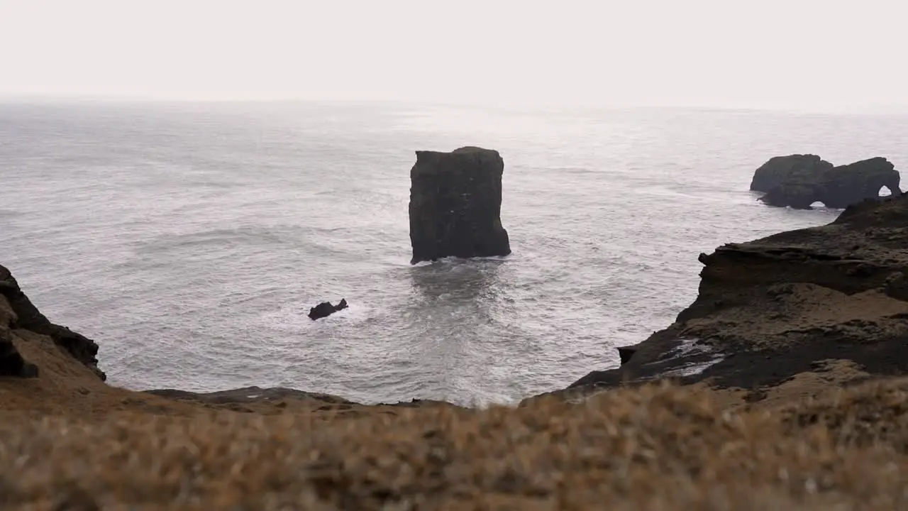 Rocky cliff washed by foamy sea in overcast weather