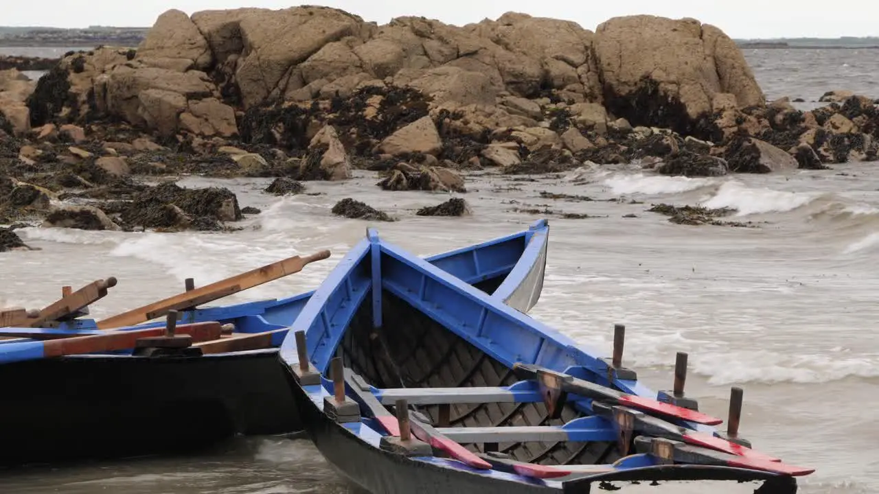 Currach boats anchored docked on shore rock in rough waves at ladies beach