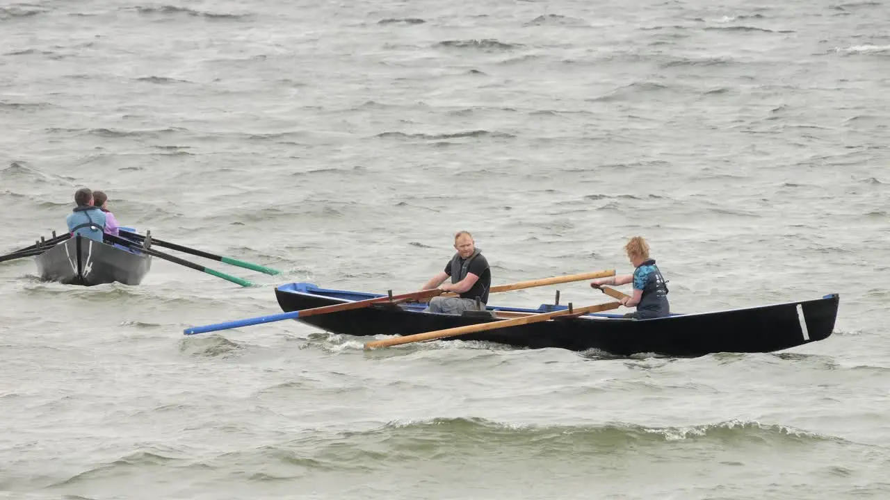 People float in water struggling to paddle currach boats through rough seas