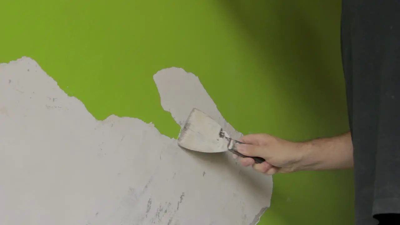 steady wide shot of a man scraping off green paint from a wall