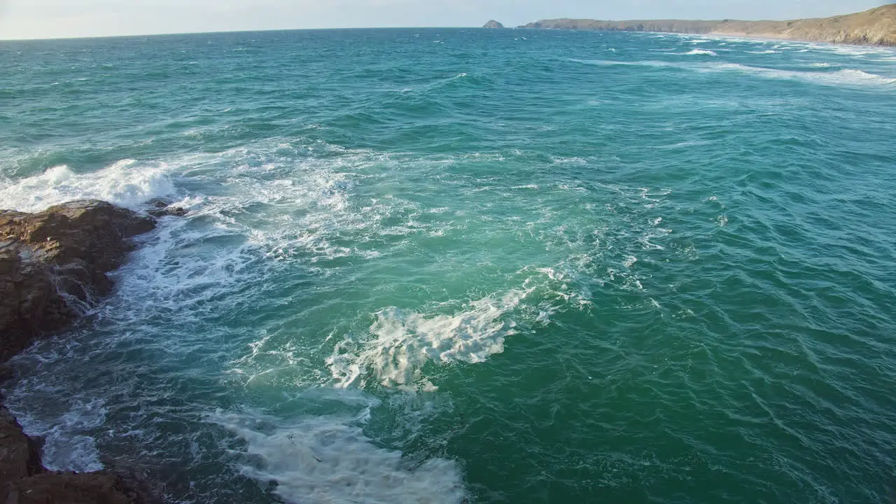 View of Foamy Turquoise Green Waves Splashing Over Coastal Rocks from Cliffside Cornwall slow motion