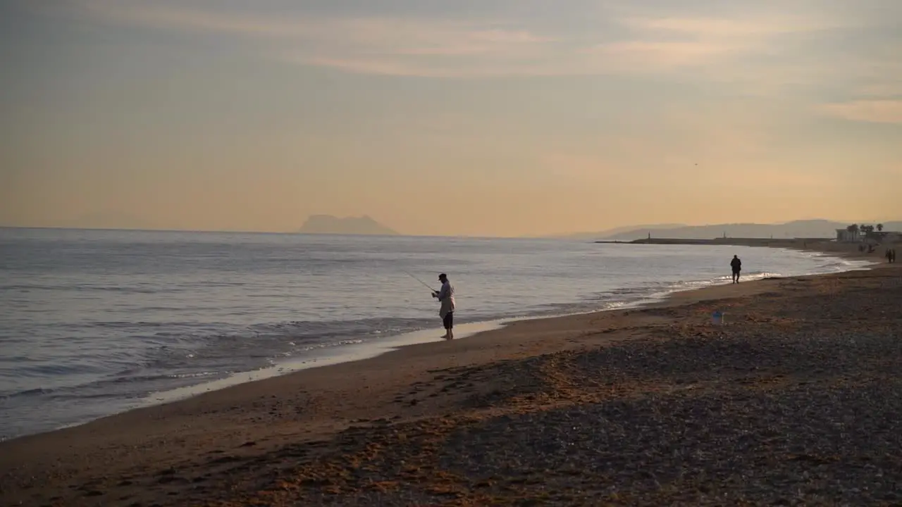 Two fisherman standing on beach during sunset and Gibraltar in distance