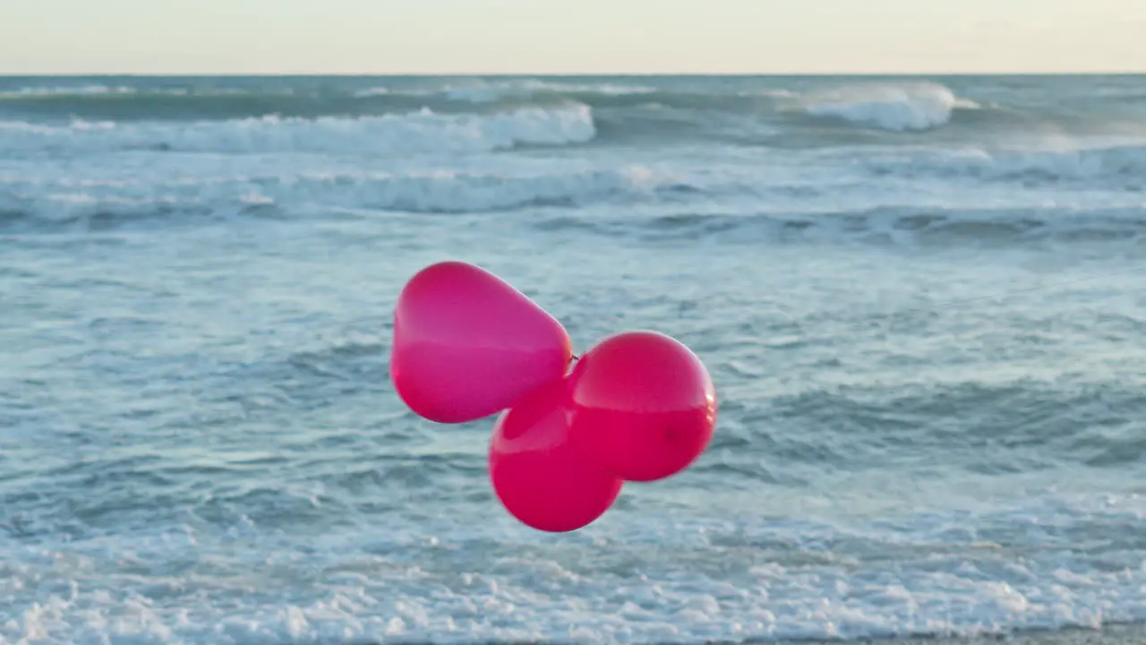 Three red balloons dance in wind as sea waves break in the background