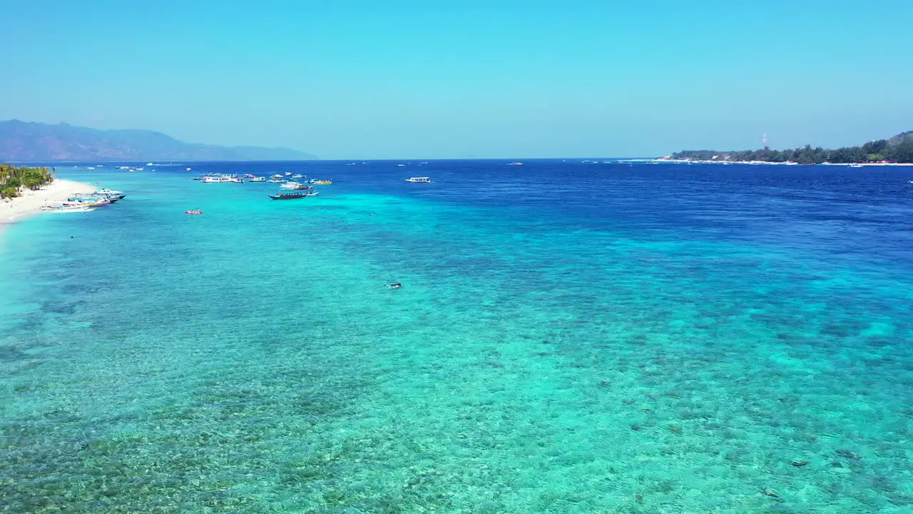 Crystal emerald water of calm turquoise lagoon with boats floating near shore of tropical island with white beach in Indonesia