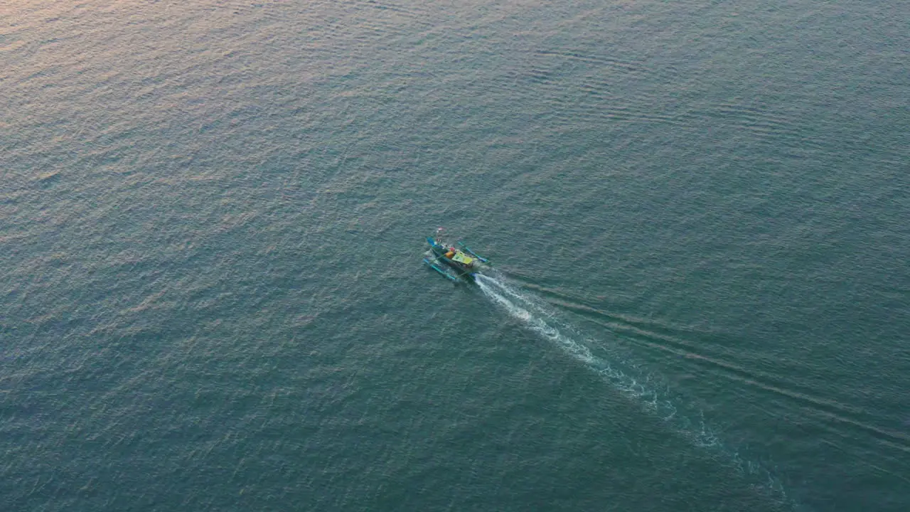 A colorful local fishing boat traveling through the tropical waters of Bali during Sunset aerial follow