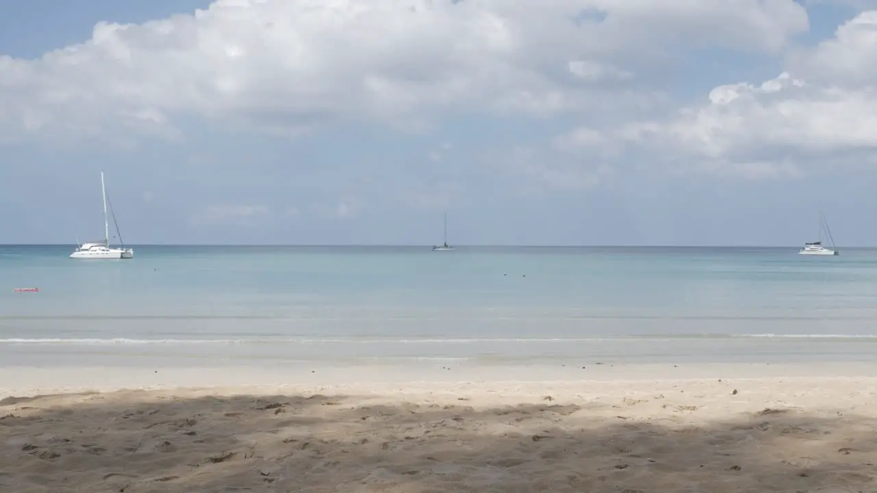 the beach with a few yachts in sea white sand and wave from peaceful sea in sunshine daytime