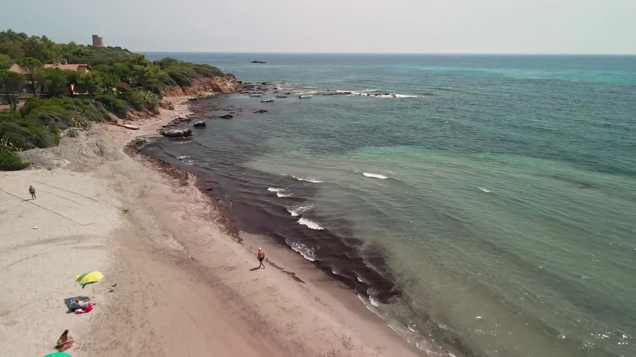 Blue Sea And Beach With Tourists Enjoying The Summer Holidays In Sardinia Italy aerial pullback