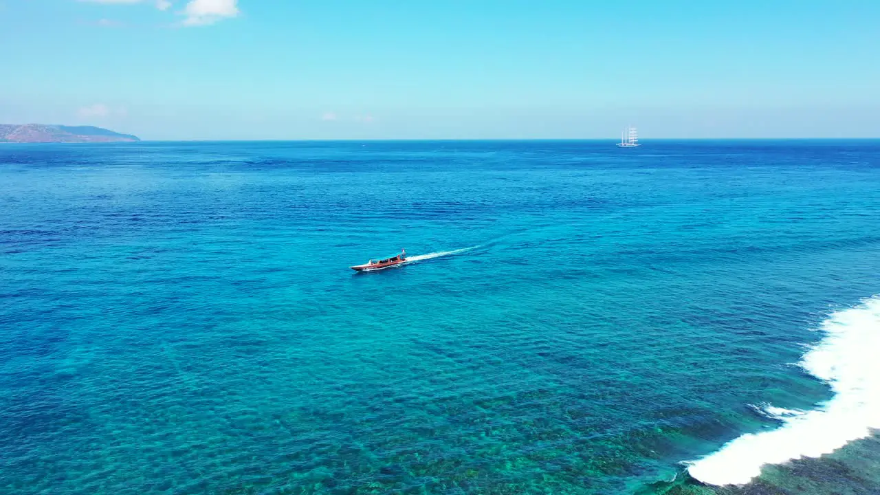 Tourist boat sailing alongside beautiful shoreline of tropical island on calm clear water of turquoise lagoon in Bali