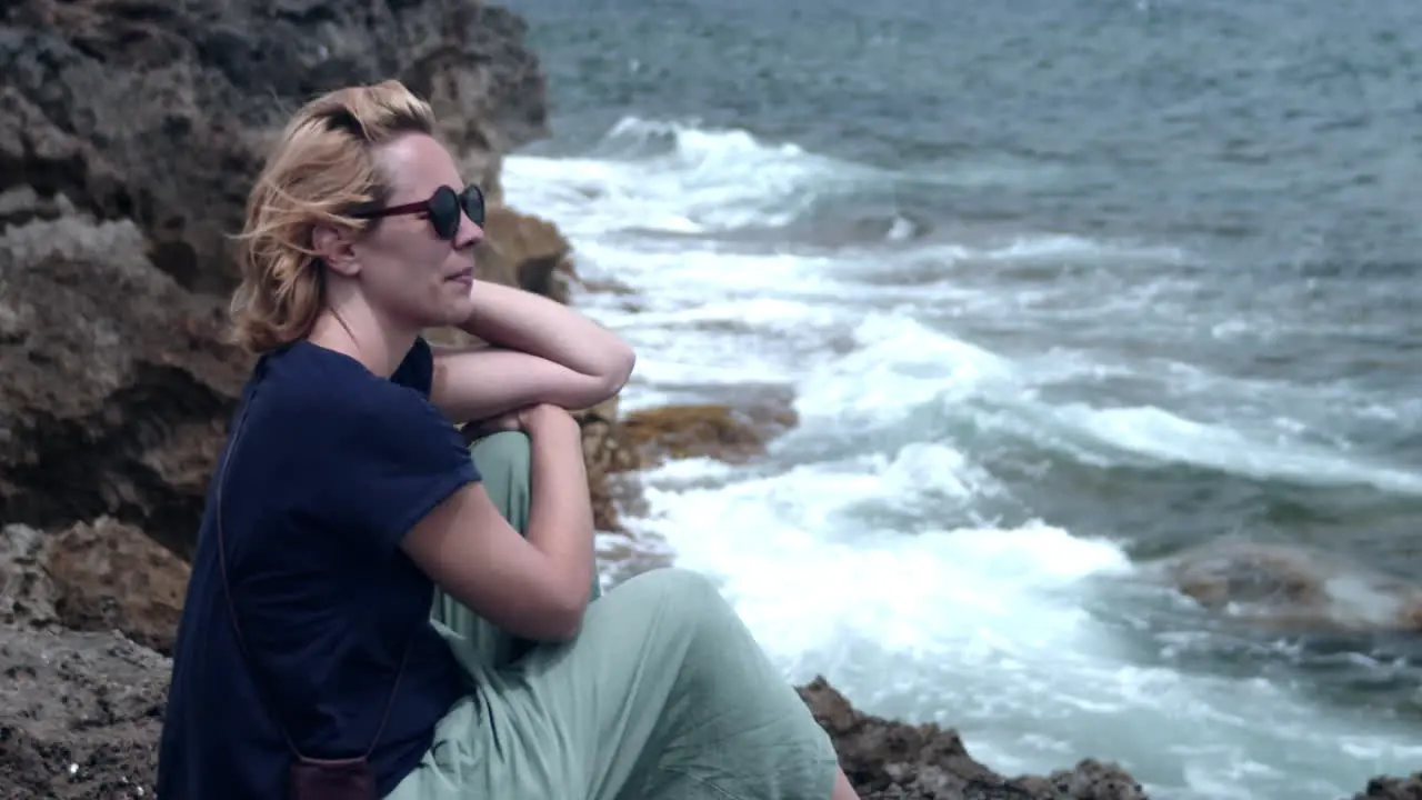 Woman sitting on cliff relaxing by the sea looking at waves Mallorca