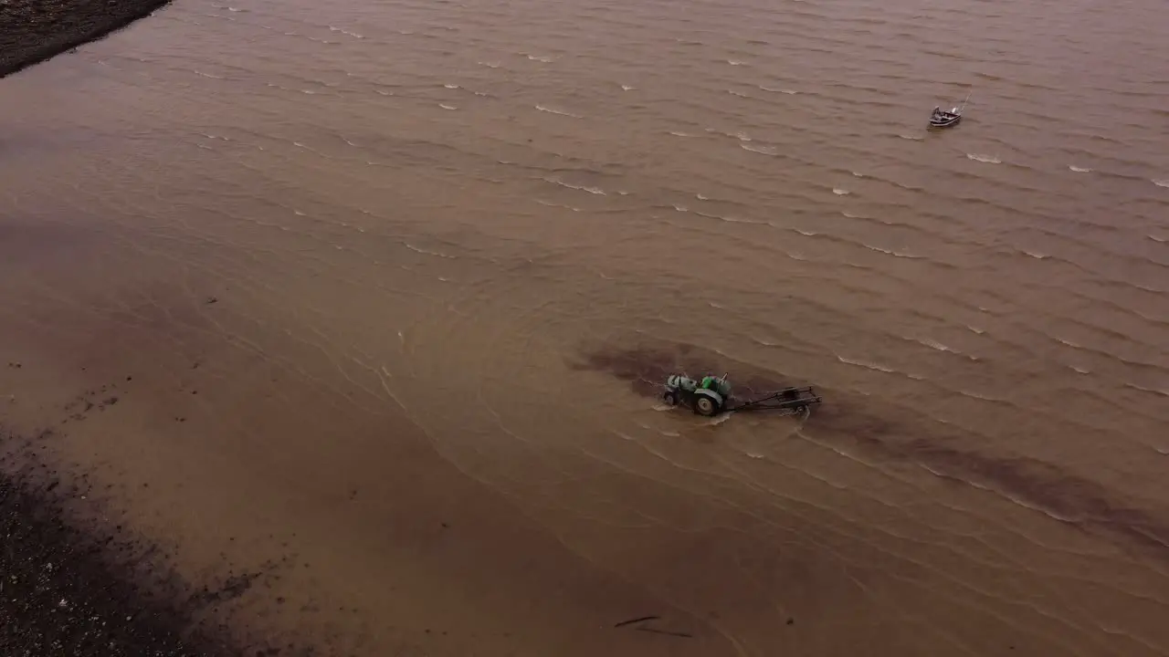 Aerial drone orbiting around tractor entering in river to take boat out of water Buenos Aires in Argentina