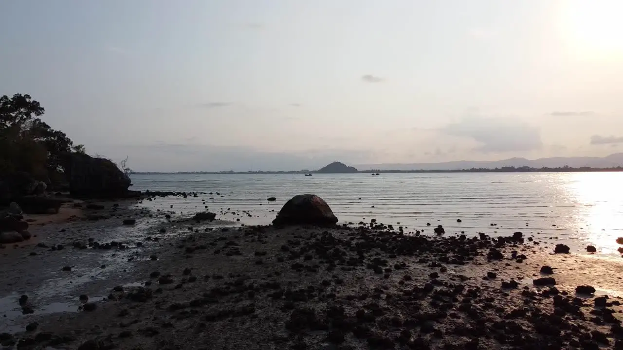 Drone travels backward above shellfish and stones on the shore at sunset in Southern Thailand Asia