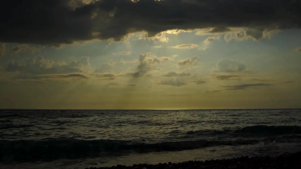 Dramatic seascape with dark clouds covering sunset and sun rays reflecting on sea surface