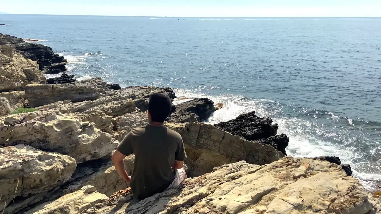 Young Man Sitting On The Rocks Enjoying The View Of Ocean At Summer In Saint-Jean-Cap-Ferrat France