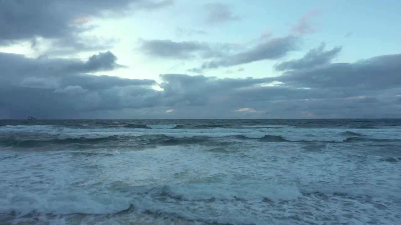 Aerial view low over waves crashing the coast of Spain gloomy evening reverse drone shot