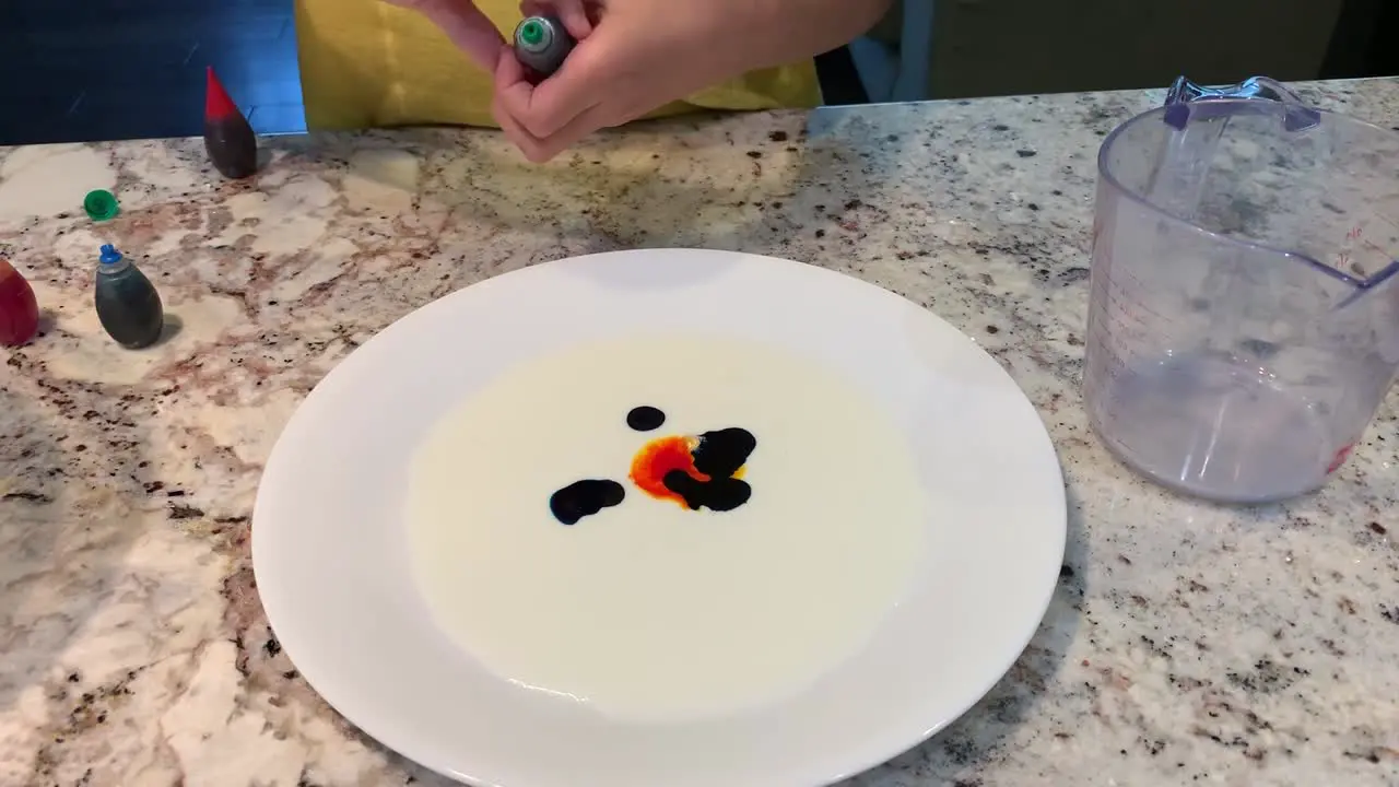 Small hands dropping different colors of food coloring onto a plate of white milk