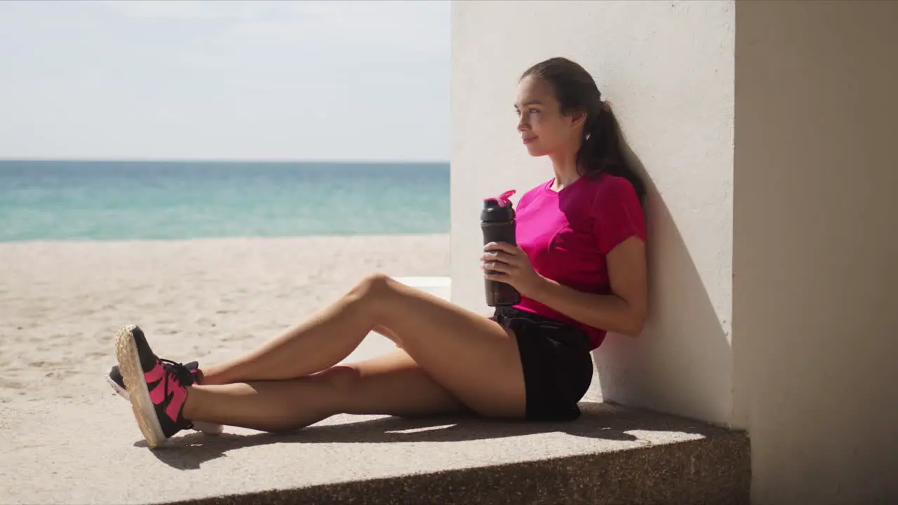 Sporty woman with bottle of water relaxing after workout on beach