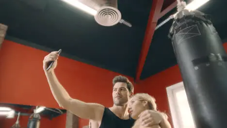 Cheerful couple hugging for mobile selfie in fitness gym