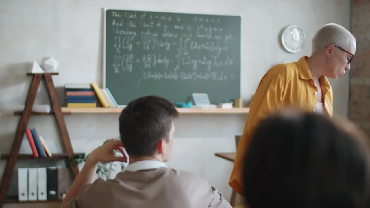 Female Teacher Walking in Classroom and Helping Students on Lesson