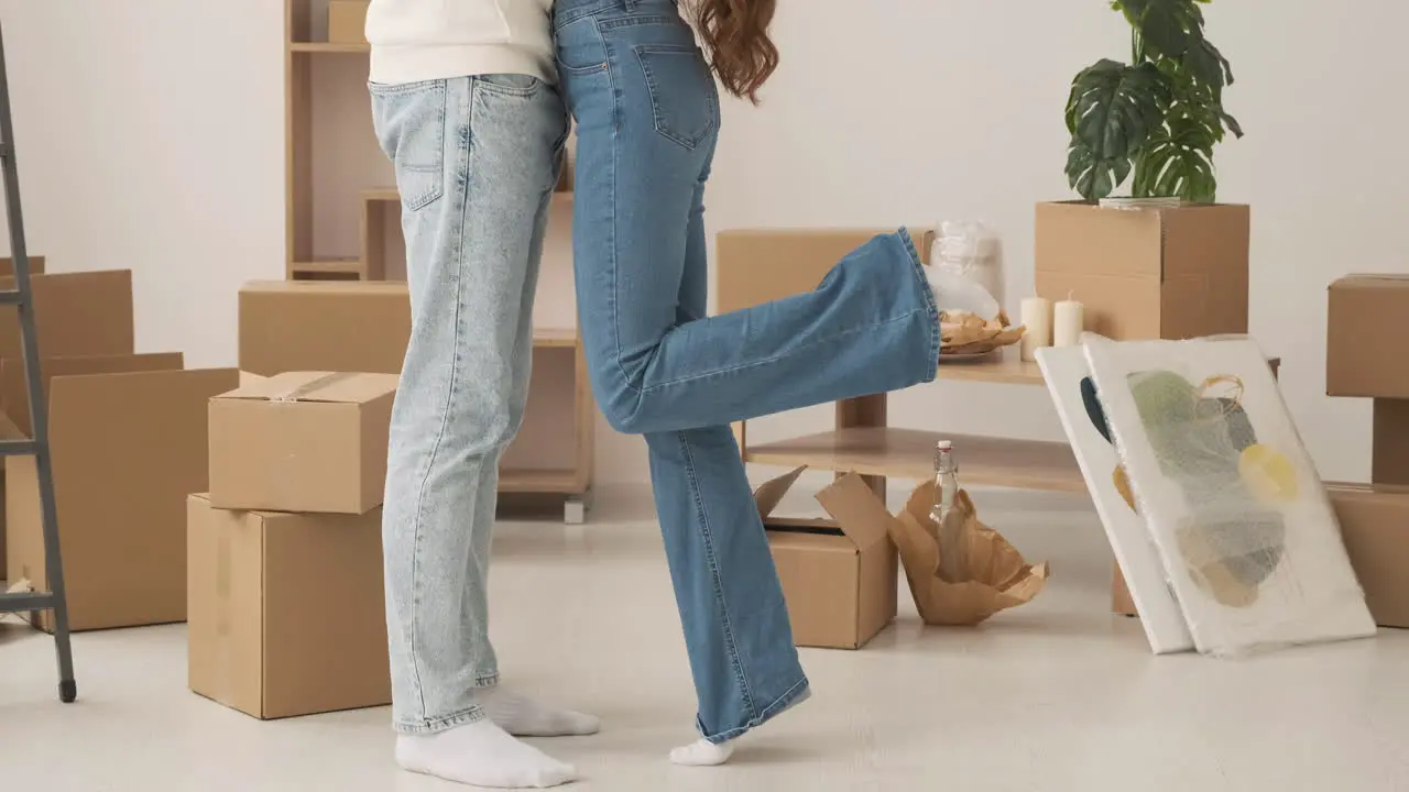 Close Up Of Legs Of Unrecognizable Couple Standing Among Cardboard Boxes In New House