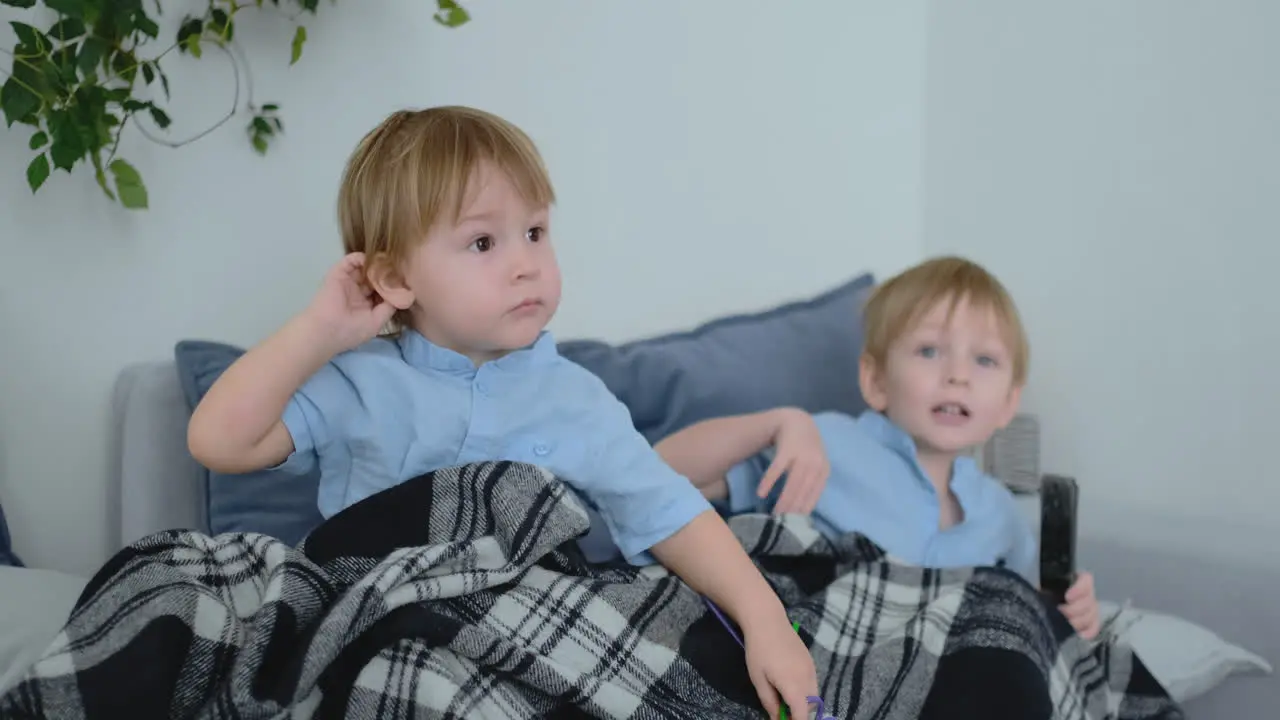 Two boys 4 and 2 years old are watching TV sitting on the couch An exciting TV show View cartoons Children watch an exciting TV show