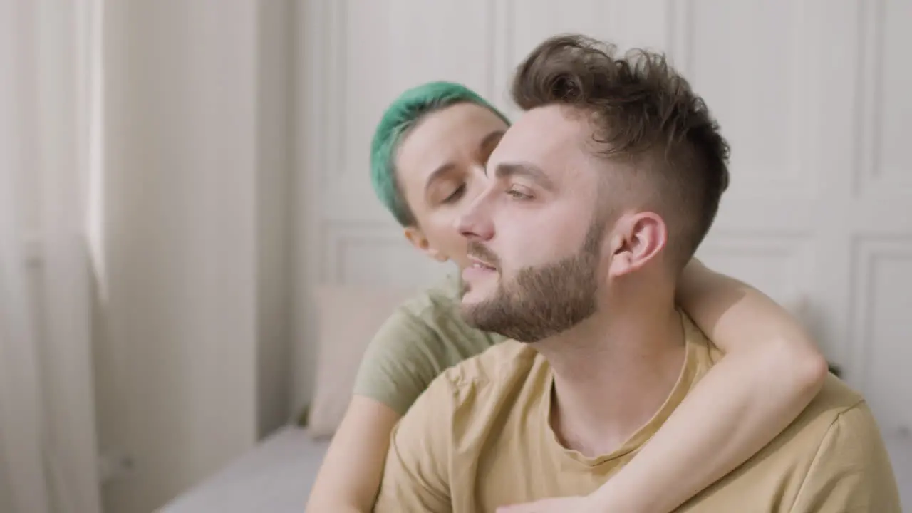 Handsome Man Sitting On The Bed While His Girlfriend Hugging Him From His Back